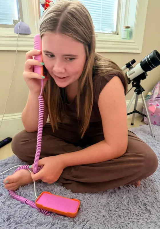 A girl sitting cross-legged on a rug, talking on a Later Alligator Lilac Tin Can landline