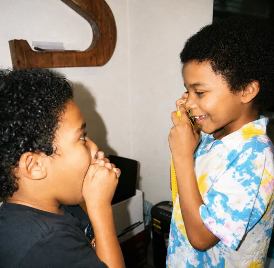 A boy talking on a Landline Lemon Tin Can while his friend giggles beside him