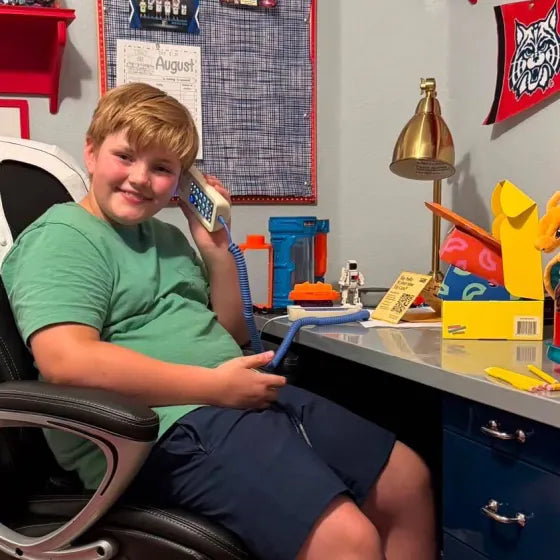 A smiling boy at his desk talking on a Static White Tin Can, a screen-free phone for kids