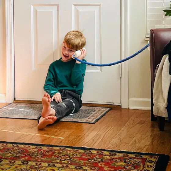 A boy sitting on the floor by the front door, on a call with his Static White Tin Can