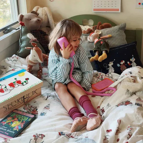 A girl on her bed among stuffed animals, chatting on a Later Alligator Lilac Tin Can