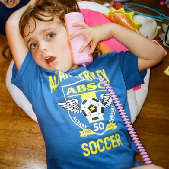 A boy in a soccer shirt lying on a beanbag, talking on a Later Alligator Lilac Tin Can